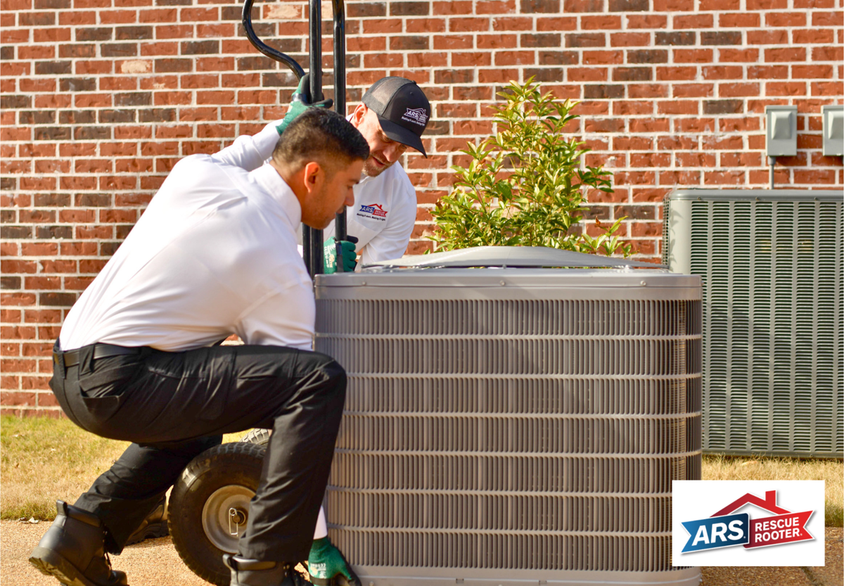 Two ARS/Rescue Rooter technicians outside of a home, hauling a new AC system with a dolly for air conditioning services. 